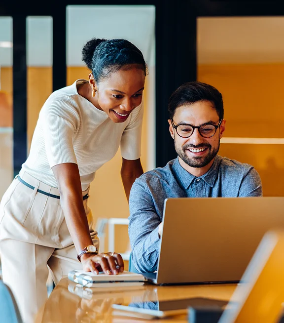 Two coworkers looking at a laptop together in a modern office