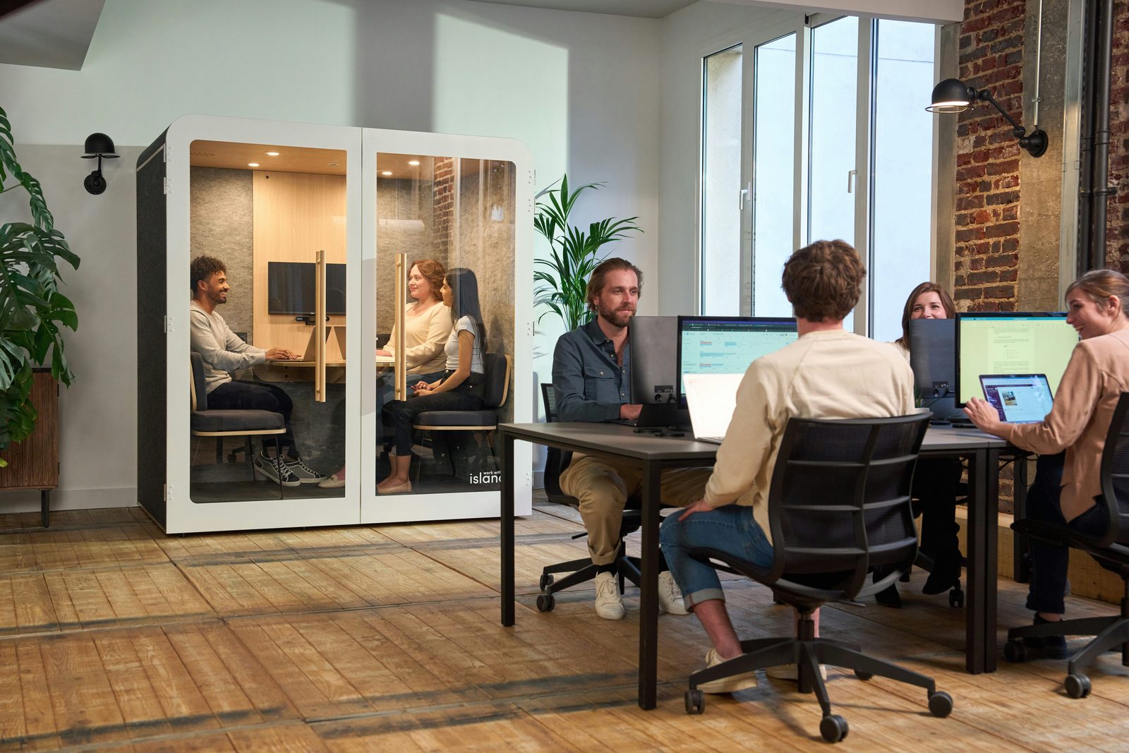 Coworkers collaborating around a table in a modern office with a private phone booth