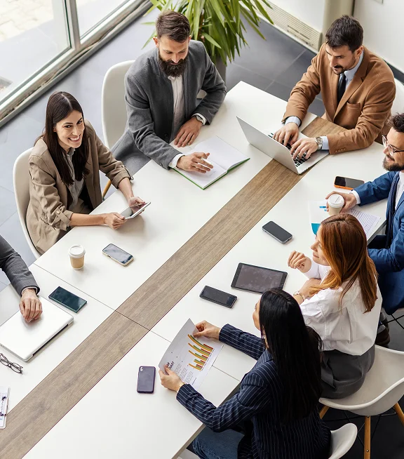 A team collaborating around a conference table with laptops and phones